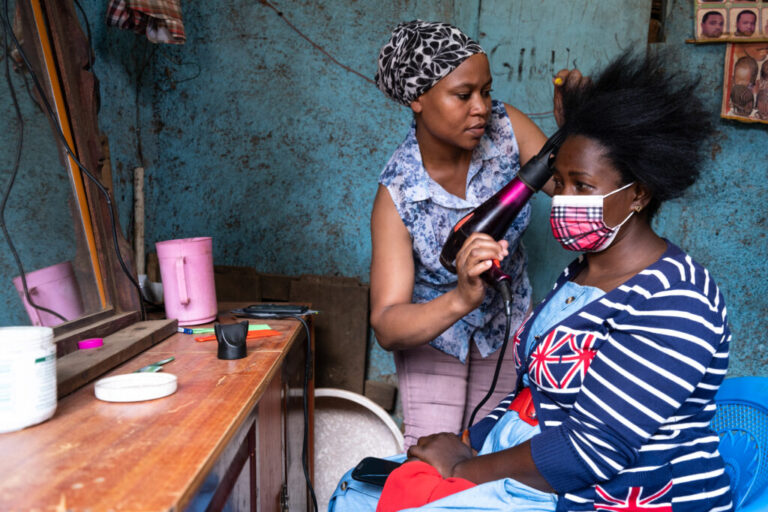 Mariam Hassan sits in front of a mirror getting her hair blow-dried by Saly Amutwayi.