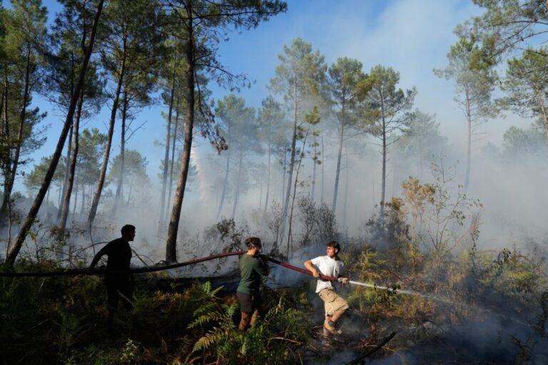 A group holds a firehose and tries to suppress a fire near Lacanau, as wildfires rage outside Bordeaux, France, Monday, July 27, 2026.