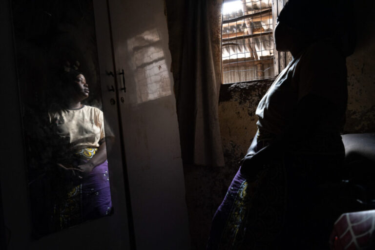 A woman stands in front of a mirror with her face turned toward a window.