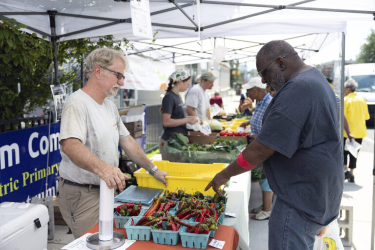 Hank Whittenberg (left), owner of Hayday Farms, helps Kenny Waddington use “Food Bucks” to pay for produce at a farmers market in Philadelphia.