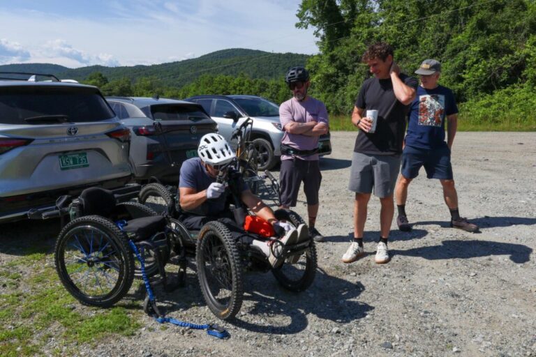 Louis Arevalo, left, straps into his adaptive mountain bike and chats with Jeff Dickson of the Vermont Mountain Bike Association, Angus McCusker with Vermont Huts and Trails, and volunteer Thatcher Hinman (all from left) ahead of a trail accessibility assessment in Randolph, Vermont, on Thursday, June 25, 2026.