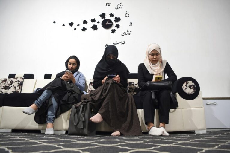 In this 2022 photo, three university students check their smartphones. In June, the Taliban announced a ban on the devices in certain sectors of society. The ripple effect is making students afraid to bring their smartphones to school.