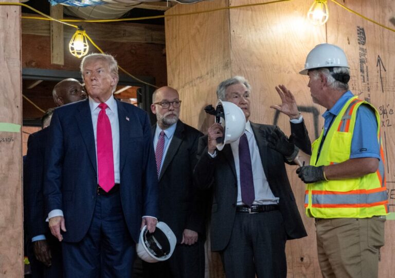 This photo shows President Trump, Federal Reserve Chair Jerome Powell and the director of the Office of Management and Budget, Russell Vought, during a tour of renovations at the Federal Reserve in Washington, D.C. Powell is speaking with the construction manager, who is wearing a fluorescent vest. Wooden boards cover many areas of the building.