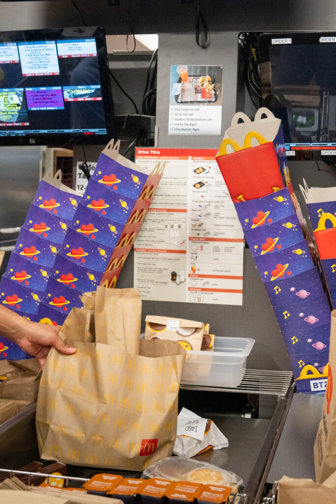 An employee reaches for a paper bag to prepare an order next to stacks of space-themed Happy Meal boxes for children.