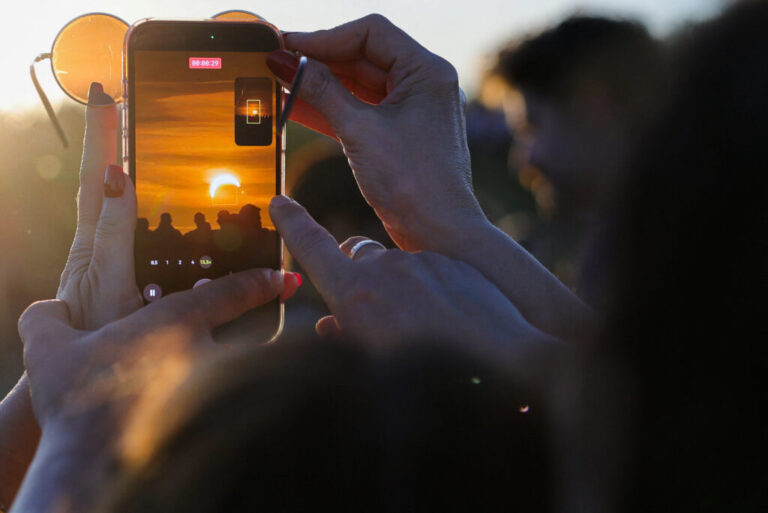 People record a video of the moon partially covering the sun during a solar eclipse, as seen from Berlin, Germany.