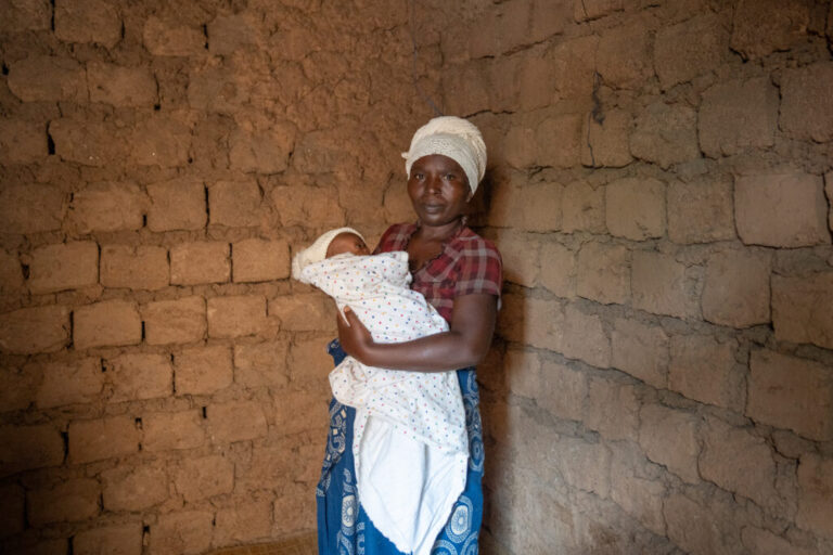 Noella Mukanoheli, 42, lost five liters of blood while she was in labor with her child. She's seen holding her infant, swaddled in a blanket, in a brick building.