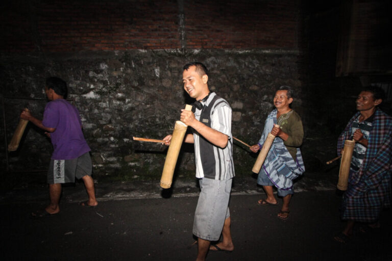 Four Indonesian Muslim men walking outdoors in the dark use sticks to strike kentongans, which are traditional wooden drums, to wake people up for sahur, the early-morning pre-fast meal during Ramadan, on July 3, 2014, in Semarang, Central Java.