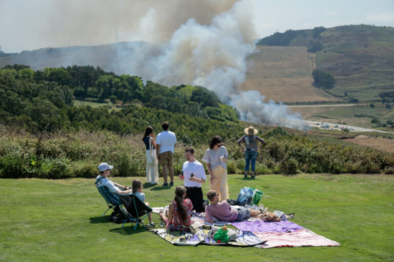 People watch as a wild fire climbs a hill near where thousands are set to gather for the total solar eclipse at El Monte De San Pedro park  in A Coruna, Spain.