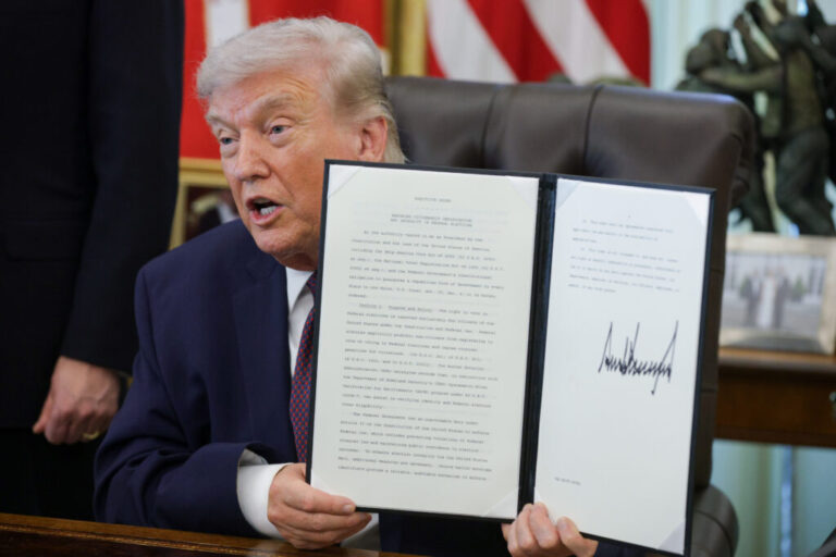 Seated at a desk in the White House's Oval Office in March, President Trump holds up an executive order calling to restrict mail-in voting.
