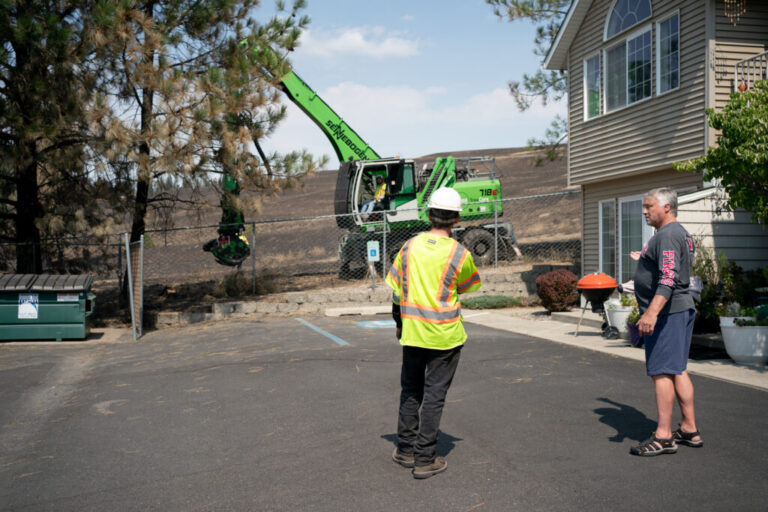 Don Simpson talks with service workers cutting down damaged trees in front of his apartment in Spokane, Wash. on August 14, 2026. During the fire, Simpson helped four residents from the Brookdale Nine Mile Nursing Facility evacuate during the Spokane Complex Fire.