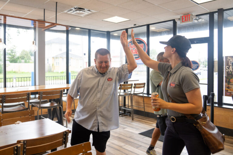 A Next Steps participant high-fives a Jersey Mike's employee while the two stand in the dining area of the sandwich restaurant. Both are wearing shirts with the Jersey Mike's logo.