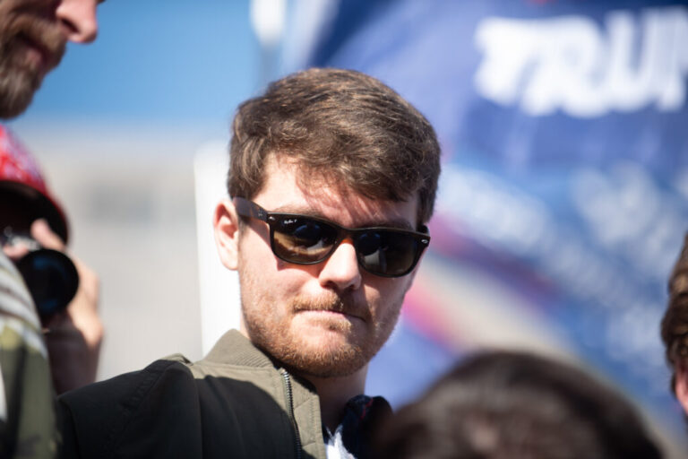 This 2020 photo shows Nick Fuentes photographed from about the shoulders up. He has brown hair and is wearing sunglasses.