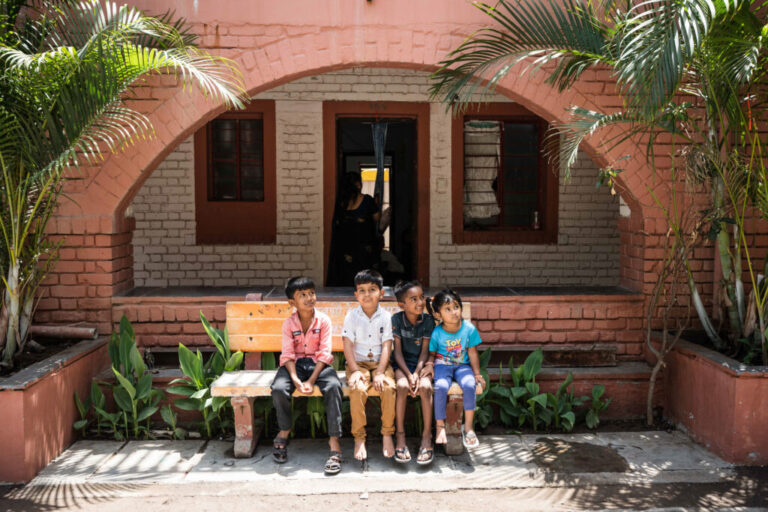 Children sit on a stone bench and relax outside the newly constructed Swapnapurti. The space and safety allows them to congregate and create a sense of community. From left to right; Aaryan