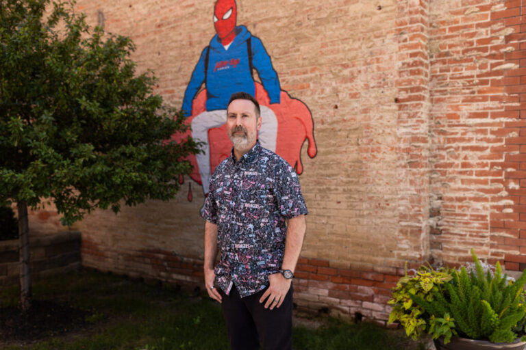 Bowker stands outside the store in front of a mural of Spiderman.