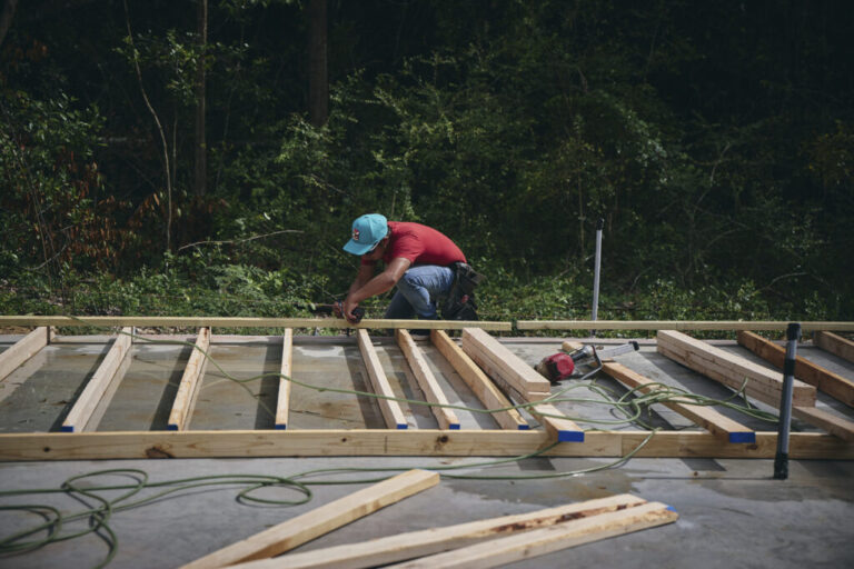 Alfonso, a 36-year-old undocumented person from Central America, crouches down near the ground as he works with pieces of lumber as part of his construction work.