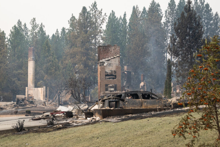 A burned car smolders in front of a burned out residential home in the Balboa neighborhood of Spokane, Wash., on August 2, 2026.