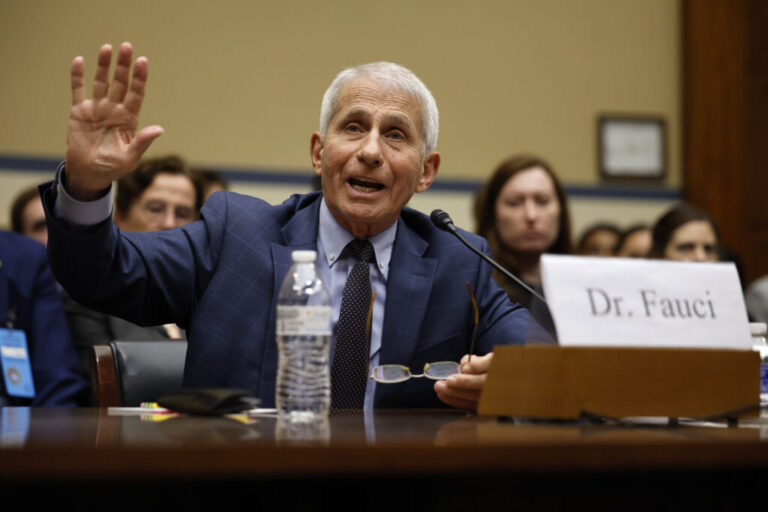Dr. Anthony Fauci is seated at a table with a microphone and a water bottle in front of him.