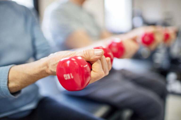 A closeup of a senior woman's forearm as she lifts a red hand weight.