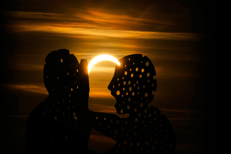 The moon partially covers the sun during solar eclipse near the Molecule Man sculpture in Berlin, Germany.