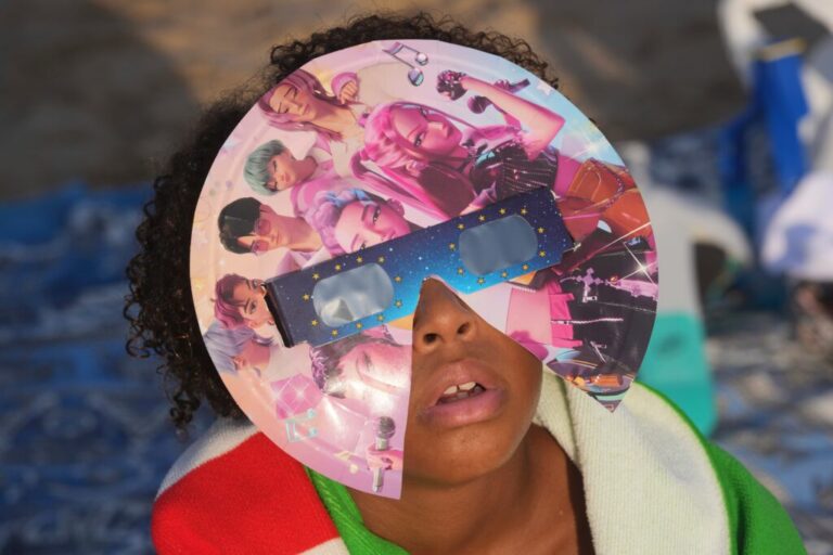 A beachgoer wearing special eclipse glasses looks up during the beginning phase of a solar eclipse