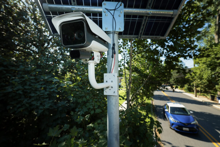 A car drives past an automatic license plate reader that has a camera mounted on a pole to monitor traffic.