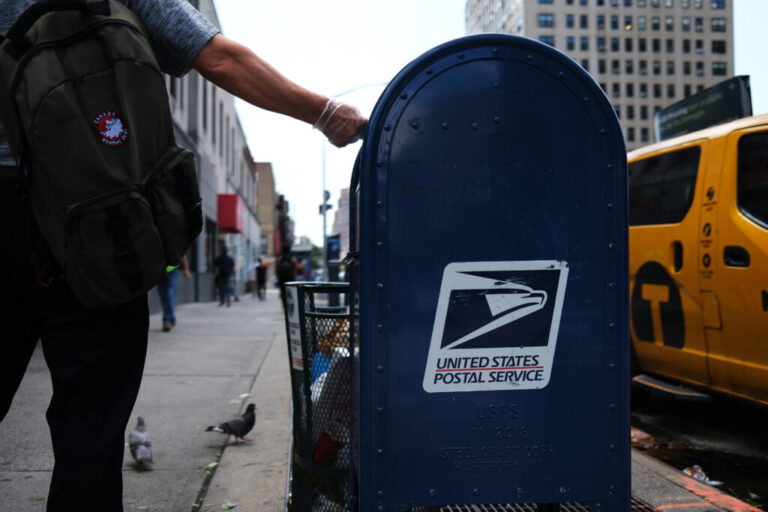 A person drops mail into a blue U.S. Postal Service collection box in New York City in 2020.