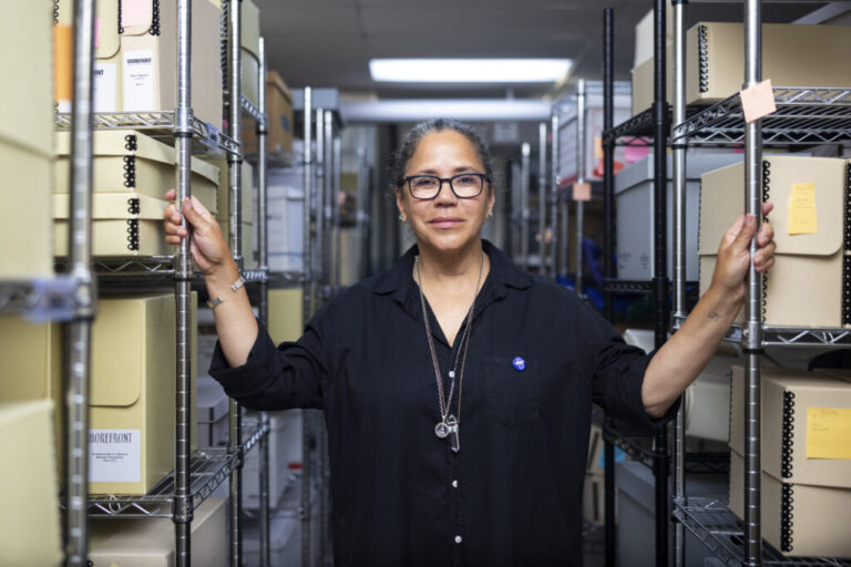 Laurice Bell stands between two rows of metal shelves holding boxes of archival materials that document the history of Black people in Evanston, Illinois.