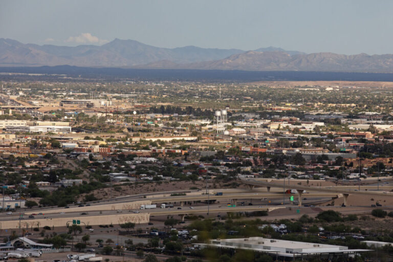 This photo shows a vista view of Tucson, Arizona, with its buildings and highways. Mountains rise up in the background.