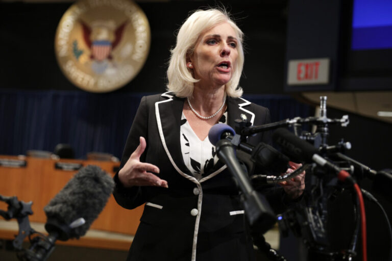 A woman stands in front of several microphones for a news briefing.