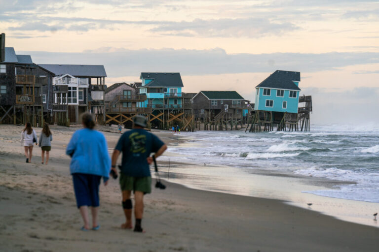 Houses perched on wooden stilts stand along the Cape Hatteras National Seashore in May. One house is tilted precariously toward the ocean.