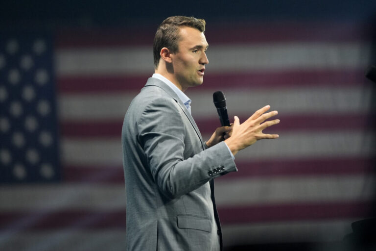 Holding a microphone and wearing a gray suit, Charlie Kirk speaks at Turning Point's Believers' Summit on July 26, 2024, in West Palm Beach, Florida.