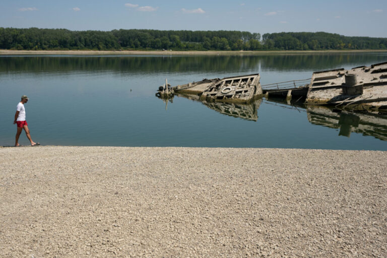 A man walks on the sandbank by the wreckage of a WWII German warship, emerged due to the drought, in front of Djerdap II, a large dam on the Danube River, between Romania and Serbia, near Prahovo, Serbia, Tuesday, Aug. 4, 2026.