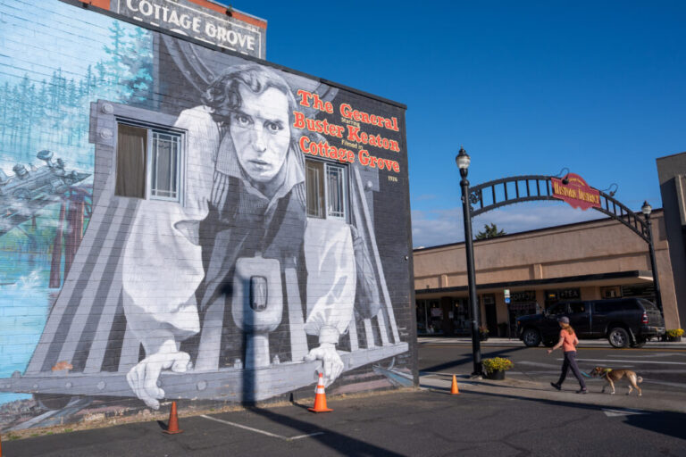 A woman walks her dog near a mural depicting Buster Keaton from his 1926 film, The General, in Cottage Grove, Ore. Fans gathered in the town to celebrate the film's centennial with a conference, a look alike contest, 1920s costume party and tours of film locations.