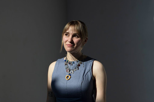 This portrait shows Jo Strogatz photographed from about the waist up. She's wearing a gray sleeveless outfit and a necklace.