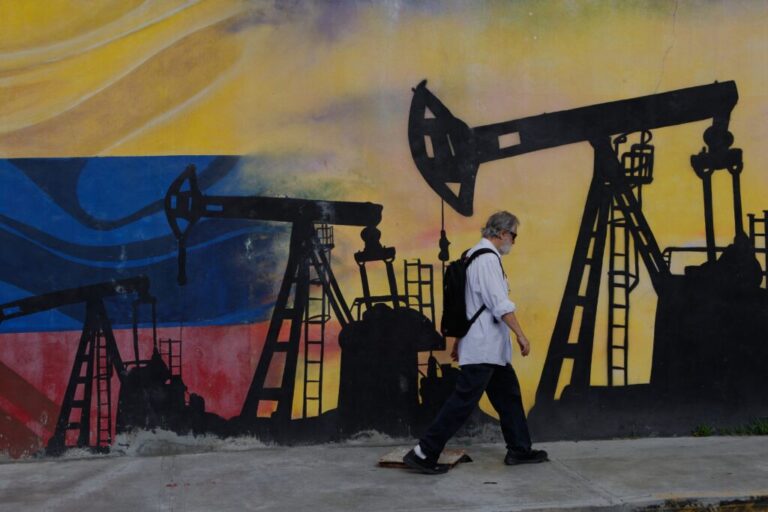 A pedestrian wearing a backpack walks past a mural featuring oil wells.