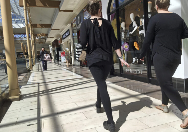 People walk inside a mall, past a row of stores.