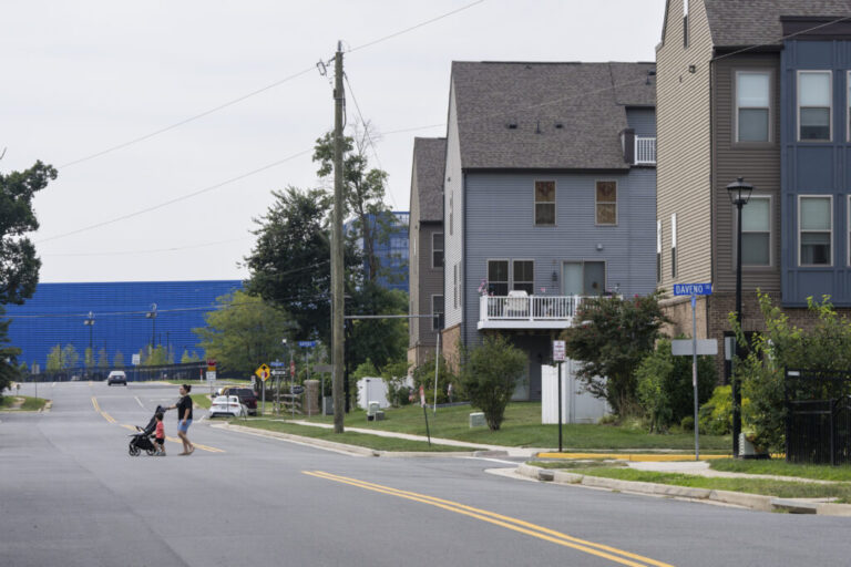 The Vantage VA2 data center, in a long blue building, sits in the background, with multistory residential buildings in the foreground, in Sterling, Virginia.