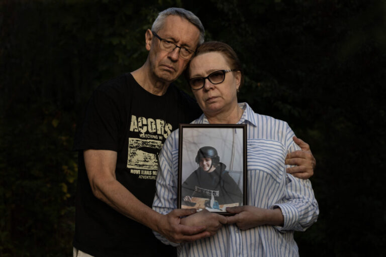Andriy Kuvshynov (left) and Iryna Mamaysur hold a framed portrait of their daughter, Oleksandra Kuvshynova, in 2024. Kuvshynova is wearing a helmet and a protective vest that says