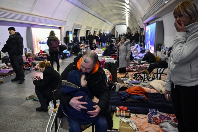 Sergyi Badylevych kisses his young child, who is in his lap while Badylevych is seated on a chair, as his wife, Natalia Badylevych, stands nearby in an underground metro station used as bomb shelter in Kyiv on March 2, 2022.