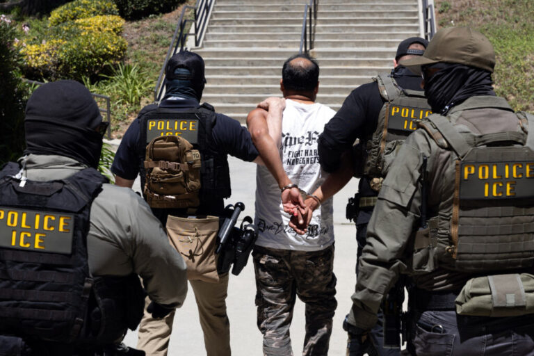 Four Immigration and Customs Enforcement agents walk a detainee out of the Ventura County Government Center in Ventura, California, on July 27. The individuals are photographed with their backs to the camera, and the detainee is handcuffed behind his back. The agents are wearing bulletproof vests that say