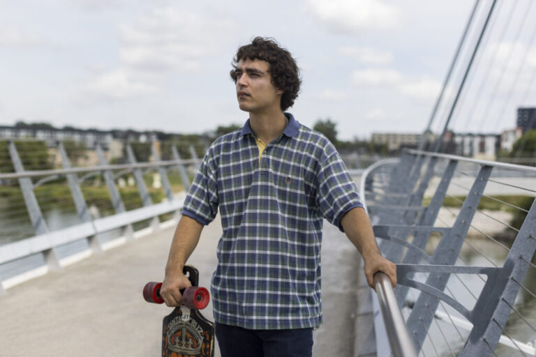 Launderville stands on a bridge while holding a skateboard.