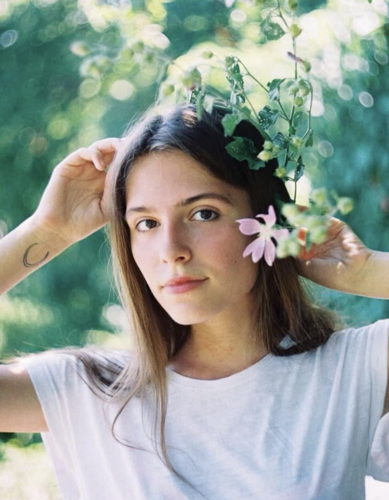 In this 2021 photo of Oleksandra Kuvshynova, she is holding a flower near her face and wearing a white shirt.