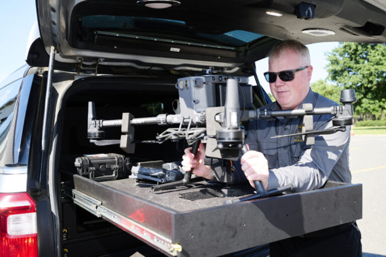Kevin Fennessy, Chief Warrant Officer, lifts an Ocean County Sheriff's Office DJI M300T drone out of the custom-built bed of a department SUV at Robert J. Miller Airpark, the temporary home of the department, September 4, 2026. These larger drones can be used with a thermal-capable camera payload for search and rescue or with a dropper payload to aid in water rescue. Albert Yee for NPR.
