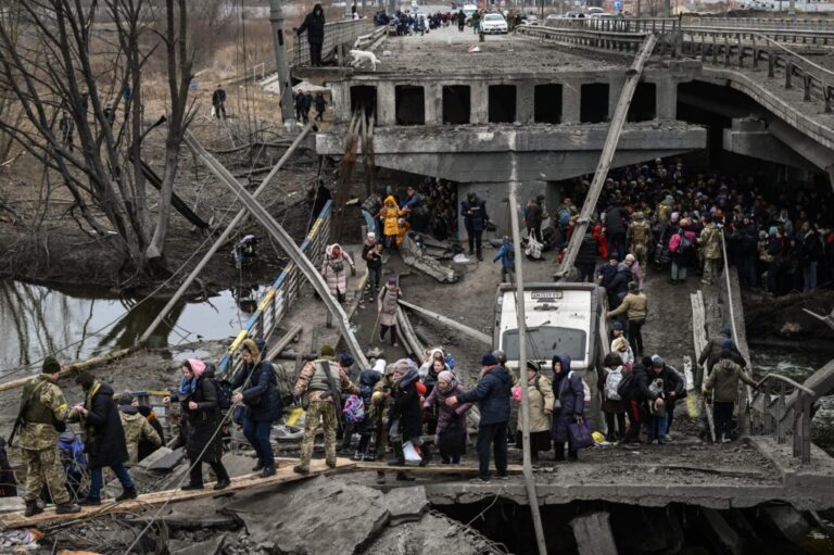 People cross a destroyed bridge as they evacuate Irpin, a suburb northwest of Kyiv, during heavy shelling and bombing on March 5, 2022. Some people are walking on wooden planks to cross over destroyed areas of the bridge.
