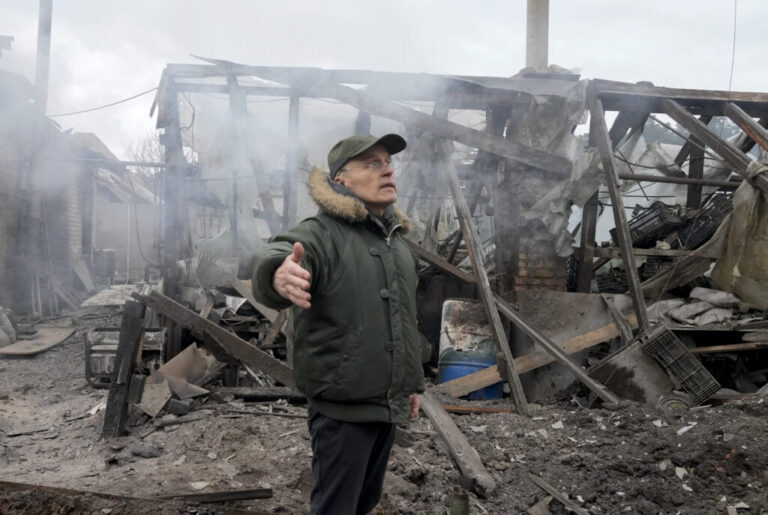 A man stands with one arm extended out to his side near a house destroyed in Russian artillery shelling in the Kyiv suburb of Horenka on March 6, 2022.