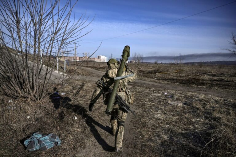 A Ukrainian serviceman wearing a camouflage uniform and carrying firearms slung on his back walks toward the front line in Irpin on March 12, 2022.